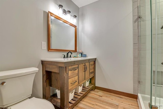 bathroom featuring wood-type flooring, a shower with door, toilet, and vanity