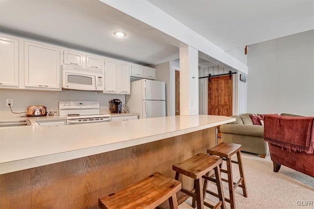 kitchen featuring kitchen peninsula, white cabinetry, a barn door, white appliances, and a kitchen bar