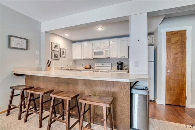 kitchen with white appliances, white cabinetry, sink, kitchen peninsula, and a breakfast bar area