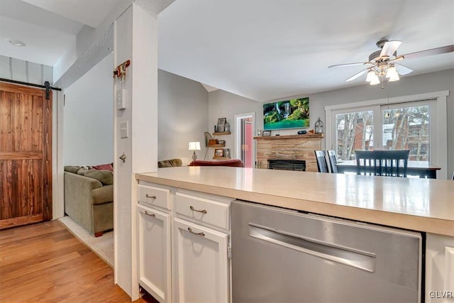 kitchen with white cabinetry, ceiling fan, stainless steel dishwasher, light hardwood / wood-style flooring, and a barn door