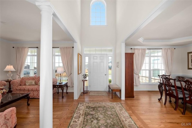 entryway featuring crown molding, light wood-type flooring, and ornate columns