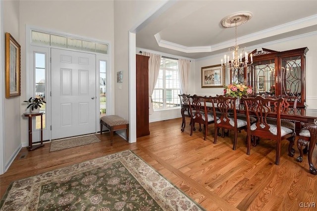 entrance foyer with ornamental molding, hardwood / wood-style flooring, a raised ceiling, and an inviting chandelier