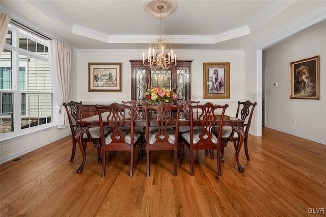 dining room featuring ornamental molding, an inviting chandelier, hardwood / wood-style floors, and a raised ceiling