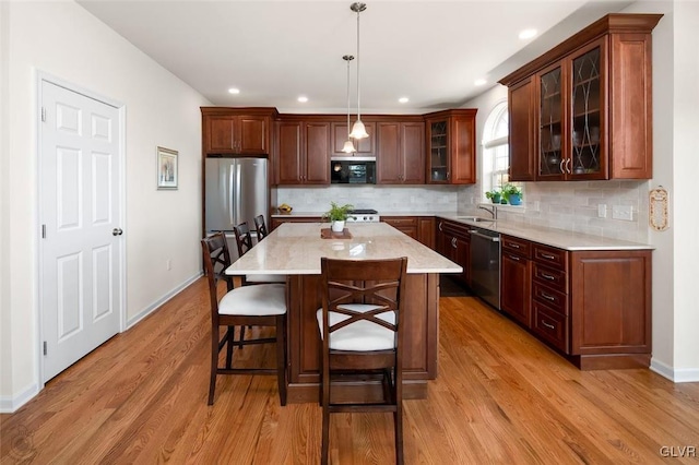 kitchen featuring pendant lighting, a center island, stainless steel appliances, tasteful backsplash, and light wood-type flooring