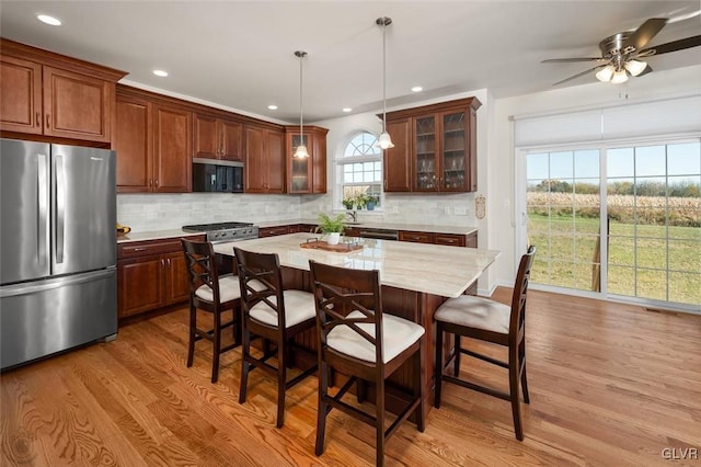 kitchen featuring light hardwood / wood-style flooring, decorative light fixtures, a wealth of natural light, a kitchen island, and stainless steel appliances