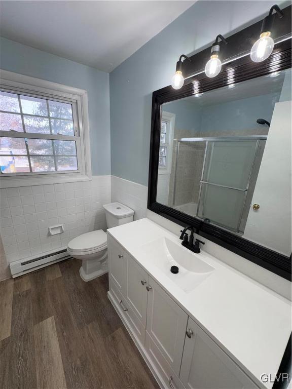 bathroom featuring wood-type flooring, baseboard heating, tile walls, a shower with shower door, and vanity