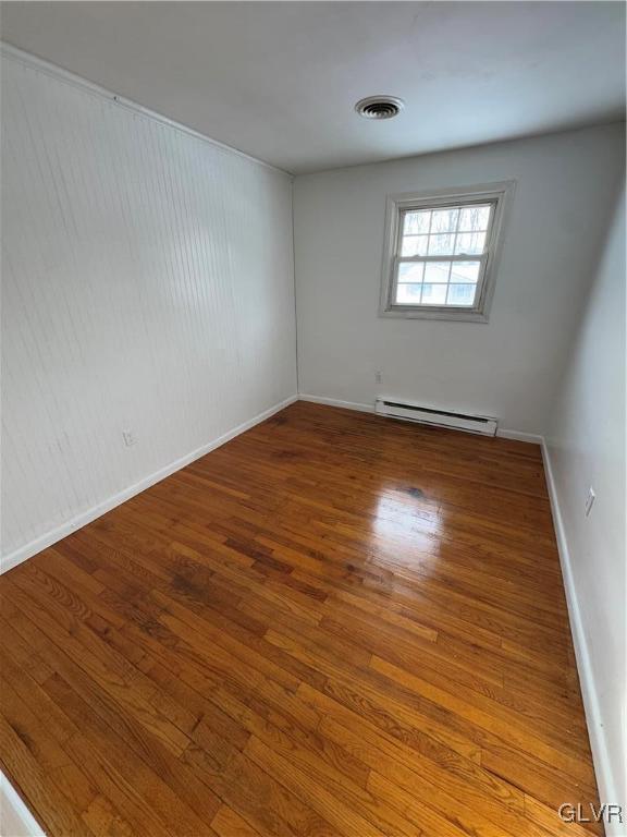 empty room with hardwood / wood-style floors and a baseboard heating unit