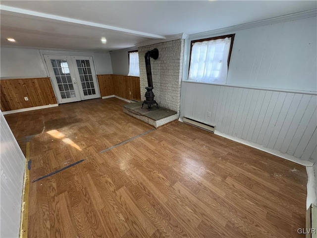 unfurnished living room with baseboard heating, french doors, hardwood / wood-style flooring, a wood stove, and wood walls