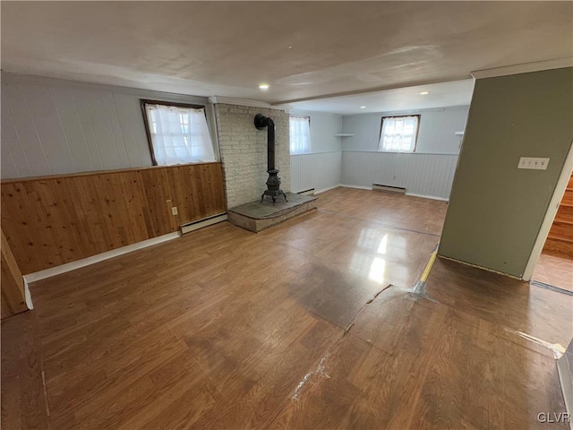 basement featuring a wood stove, wood walls, a baseboard heating unit, and hardwood / wood-style flooring