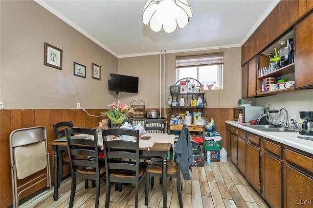 dining room featuring crown molding, light hardwood / wood-style floors, wooden walls, and sink