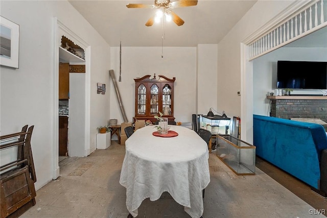 dining room with ceiling fan, a brick fireplace, and concrete flooring