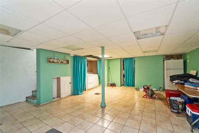 basement featuring tile patterned flooring, a paneled ceiling, white fridge, and washer / clothes dryer