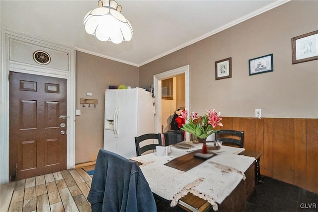 dining area featuring ornamental molding, light hardwood / wood-style flooring, and wooden walls