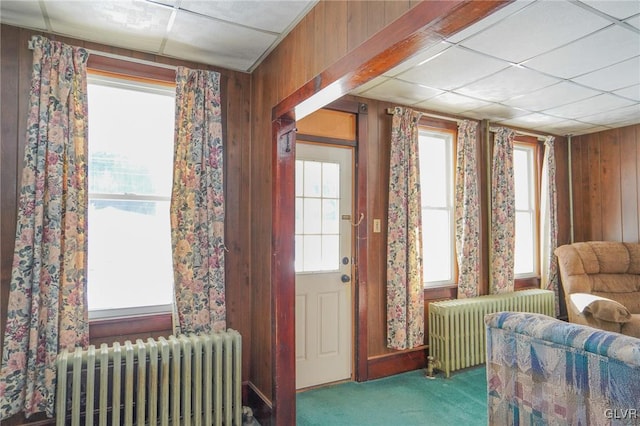 living area featuring carpet, radiator, wooden walls, and a drop ceiling