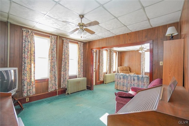 bedroom with ceiling fan, radiator heating unit, wooden walls, and carpet flooring