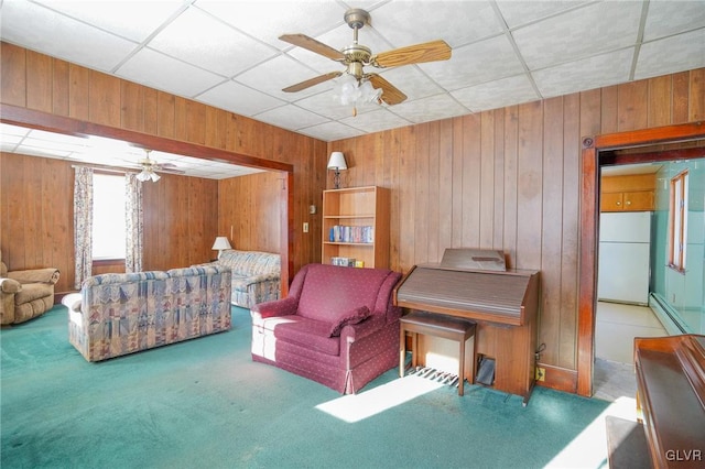 living room featuring wood walls, baseboard heating, carpet flooring, and ceiling fan