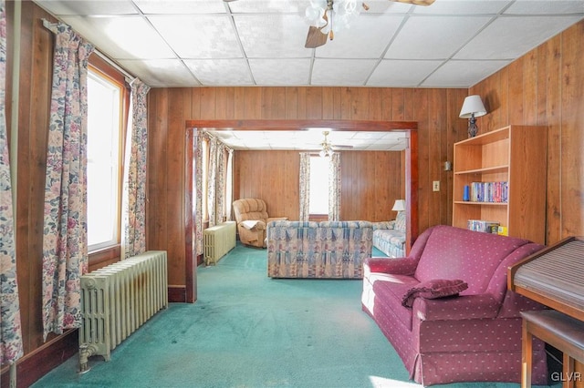 carpeted living room featuring ceiling fan, radiator heating unit, and wooden walls