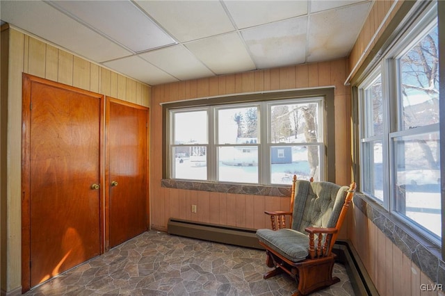 sitting room with baseboard heating, a paneled ceiling, wooden walls, and a healthy amount of sunlight