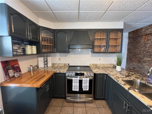 kitchen featuring backsplash, custom range hood, light stone countertops, and stainless steel range with electric cooktop