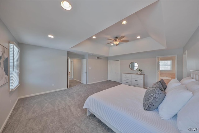 carpeted bedroom featuring ceiling fan, connected bathroom, a tray ceiling, and a closet