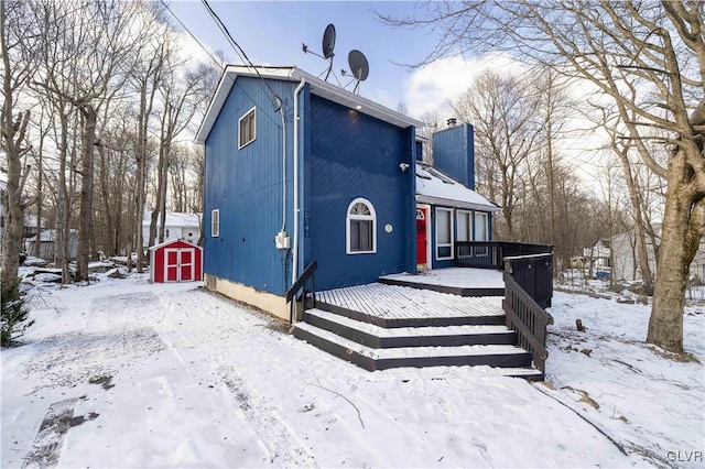 snow covered property featuring a deck and a storage shed