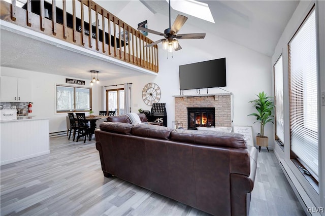 living room featuring ceiling fan, light wood-type flooring, a fireplace, high vaulted ceiling, and a skylight