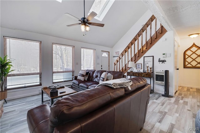 living room with a textured ceiling, light wood-type flooring, vaulted ceiling with skylight, and ceiling fan