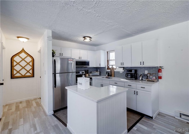 kitchen with white cabinets, appliances with stainless steel finishes, a kitchen island, sink, and light wood-type flooring