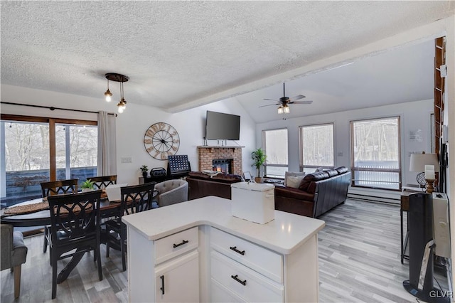 kitchen featuring a center island, a fireplace, white cabinetry, hanging light fixtures, and lofted ceiling