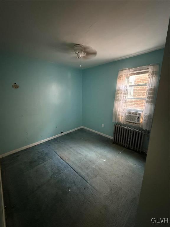 carpeted empty room featuring ceiling fan and radiator heating unit