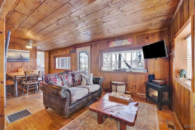 living room with wood ceiling, wooden walls, light wood-type flooring, and a wood stove