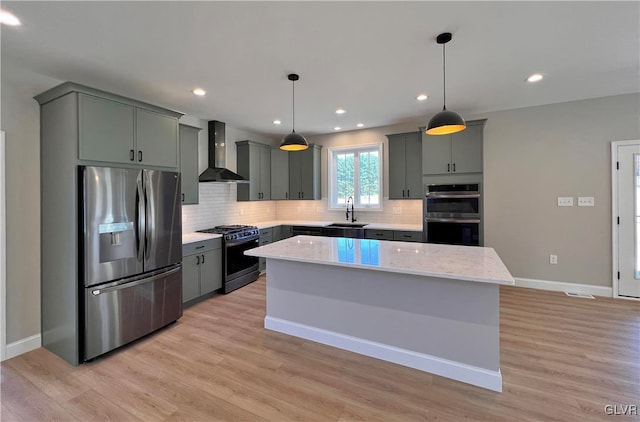 kitchen featuring a kitchen island, appliances with stainless steel finishes, decorative light fixtures, sink, and wall chimney range hood