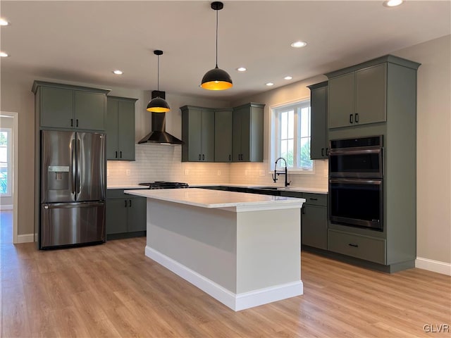 kitchen featuring wall chimney exhaust hood, a center island, pendant lighting, stainless steel appliances, and light hardwood / wood-style floors