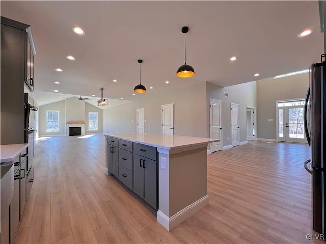 kitchen featuring vaulted ceiling, a kitchen island, decorative light fixtures, fridge, and light hardwood / wood-style flooring