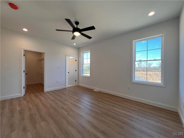 unfurnished bedroom with light hardwood / wood-style floors, a walk in closet, ceiling fan, and a closet