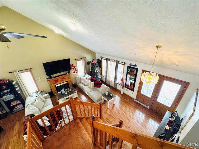living area featuring a textured ceiling, ceiling fan with notable chandelier, wood finished floors, and lofted ceiling