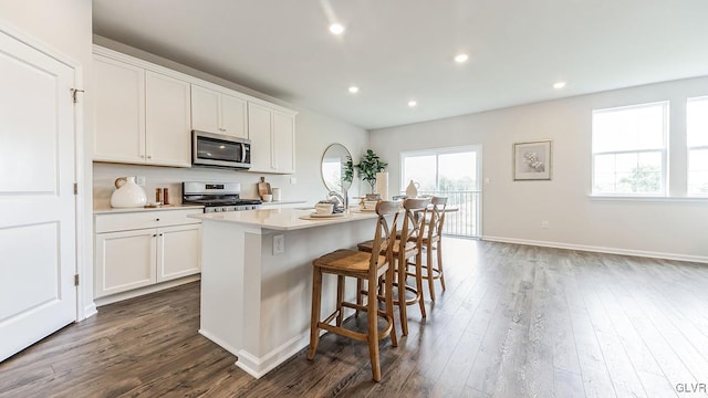 kitchen with dark hardwood / wood-style floors, a kitchen breakfast bar, an island with sink, stainless steel appliances, and white cabinets