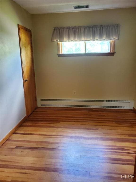 unfurnished room featuring baseboard heating, a healthy amount of sunlight, and light wood-type flooring