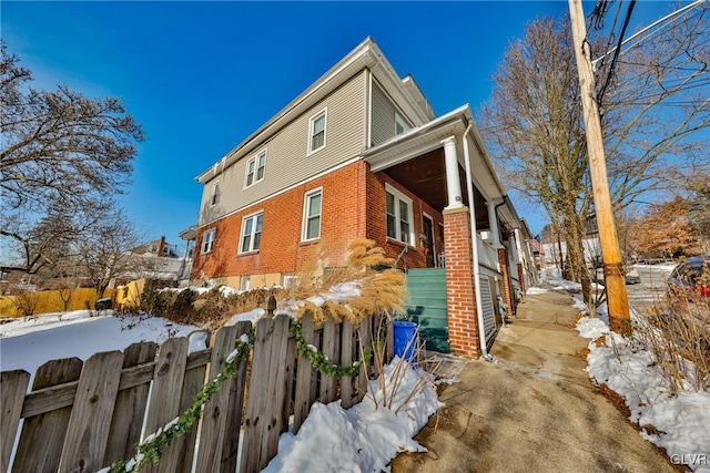 snow covered property with a fenced front yard and brick siding