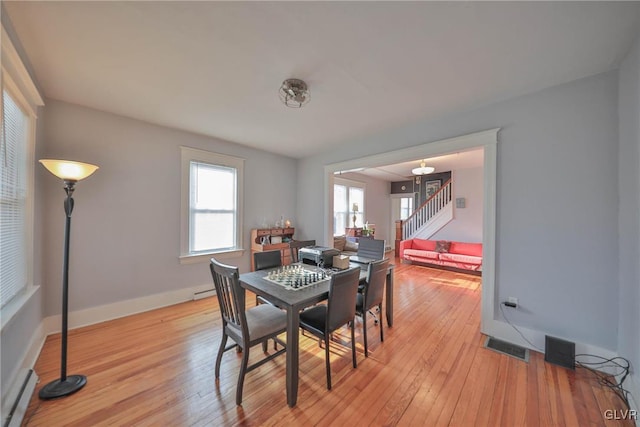 dining room featuring light wood finished floors, baseboards, stairs, and a baseboard heating unit