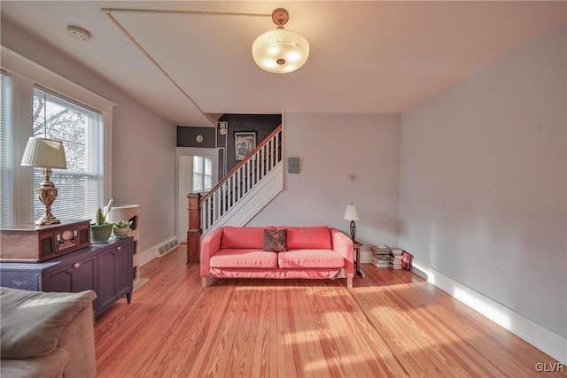 living area featuring light wood finished floors, baseboards, stairs, and visible vents