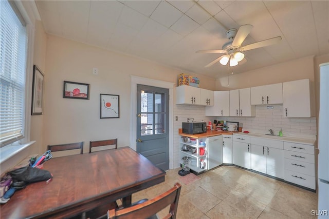 kitchen with black microwave, a ceiling fan, white cabinets, light countertops, and decorative backsplash