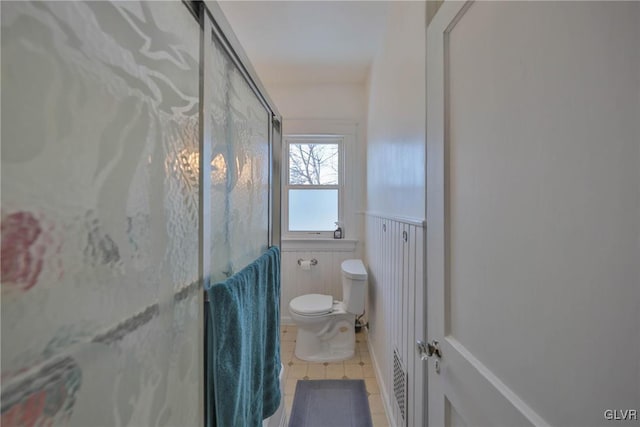 bathroom featuring a wainscoted wall, a shower stall, toilet, and tile patterned floors