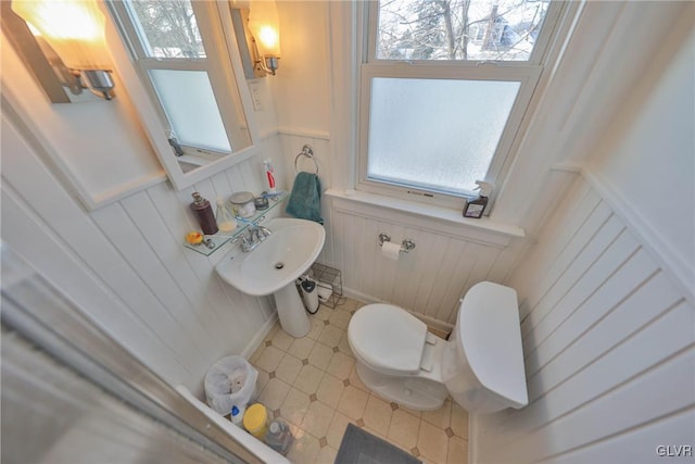 bathroom with toilet, a wealth of natural light, a sink, and a wainscoted wall