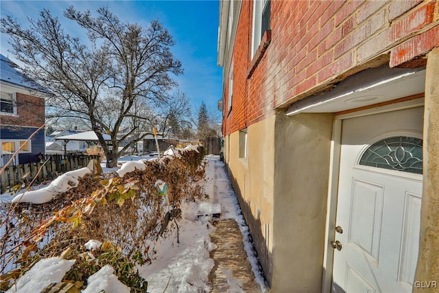 snow covered property with fence and stucco siding