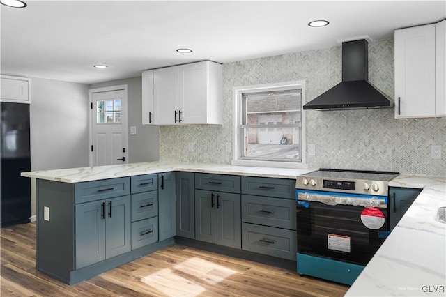 kitchen featuring black refrigerator, white cabinets, stainless steel range with electric stovetop, wall chimney range hood, and light hardwood / wood-style flooring