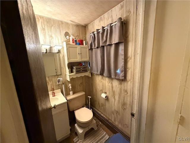 bathroom featuring vanity, wooden walls, and toilet