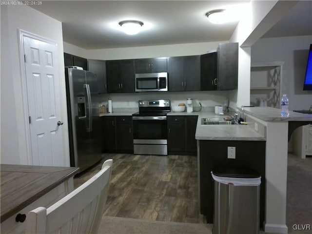 kitchen with appliances with stainless steel finishes, dark hardwood / wood-style flooring, kitchen peninsula, and sink