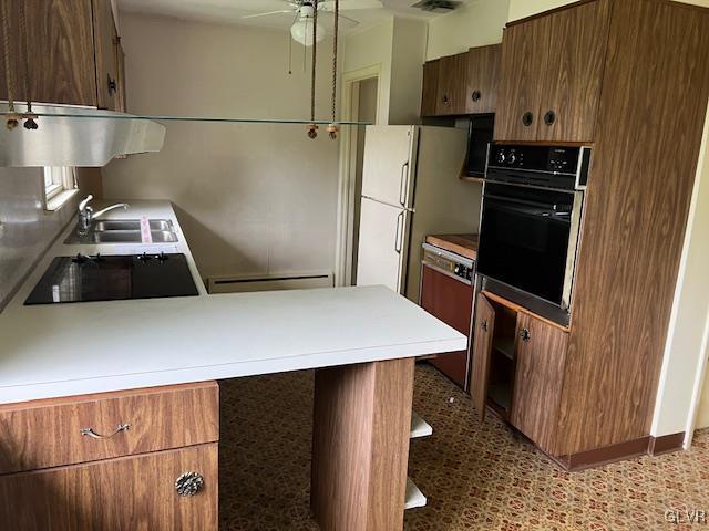 kitchen featuring black appliances, a baseboard radiator, sink, ceiling fan, and kitchen peninsula