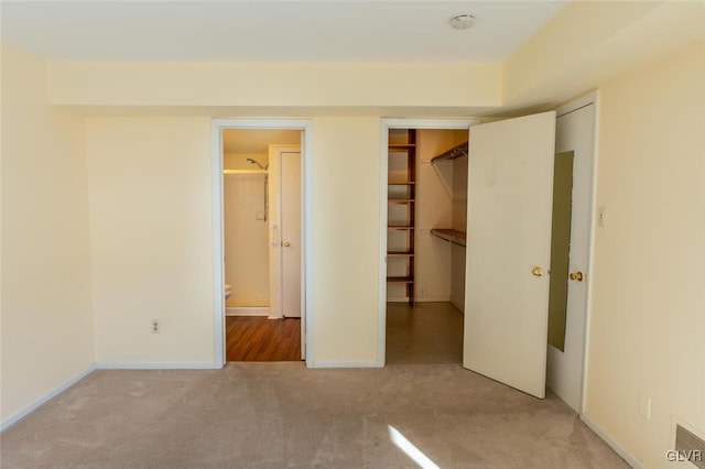 unfurnished bedroom with a walk in closet, ensuite bathroom, a closet, and light carpet